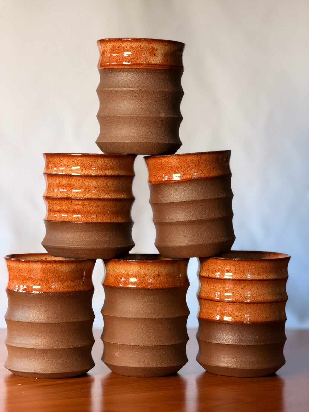 Pyramid stack of handmade stoneware water cups in rust glaze