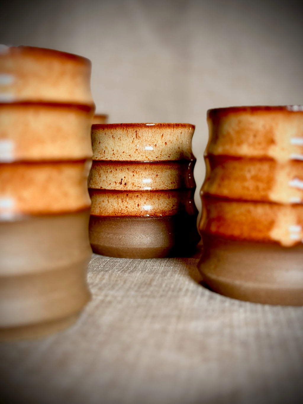 Stacks of handmade rust-glazed stoneware water cups on linen