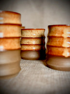 Stacks of handmade rust-glazed stoneware water cups on linen